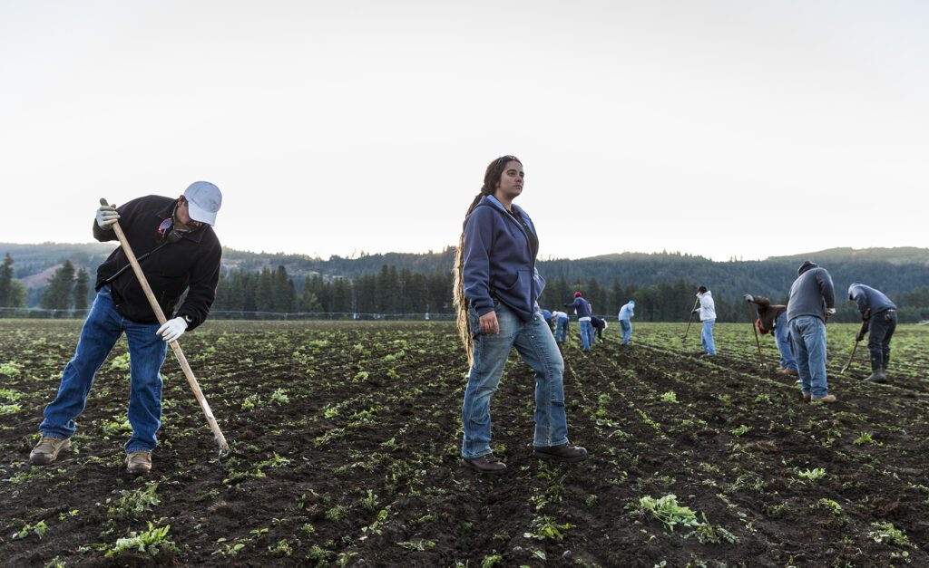 Danielle Kruse, Farm Manager, stands on soil at Trout Lake Farms with field workers tilling around her.